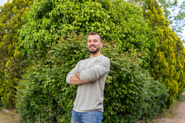 Gardener smiling with crossed arms in front of green hedge