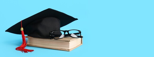 Graduation hat, book and glasses on light blue background with space for text