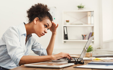 Concentrated african-american business woman working on laptop at office. Businesswoman typing something on computer while sitting at her working place, copy space, side view