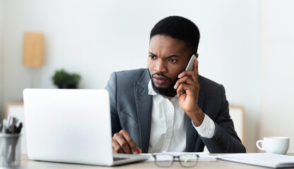 Concerned businessman talking on cell phone and looking at laptop screen, trying to reach technical support to solve issue with his computer, panorama
