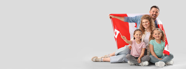 Happy beautiful family with flags of Canada sitting on grey background