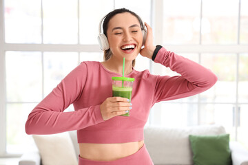 Sporty young woman in headphones with glass of vegetable juice at home