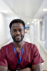 Naklejka premium Young African American man wearing scrubs and lanyard, standing in hospital corridor and smiling