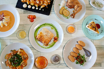 A table with many plates of food, including a plate of chicken. There are also bowls and spoons on the table