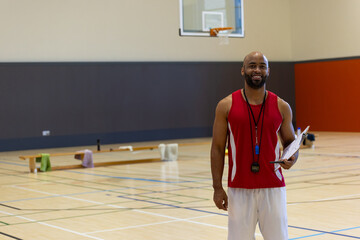 African American man coaching basketball in gym with clipboard, stopwatch and whistle, copy space