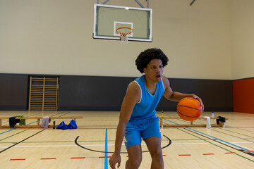African American male athlete dribbling basketball on gym court, with bench and gear, copy space
