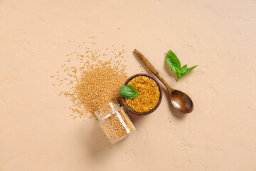 Wooden bowl of Dijon mustard with basil and seeds on beige background