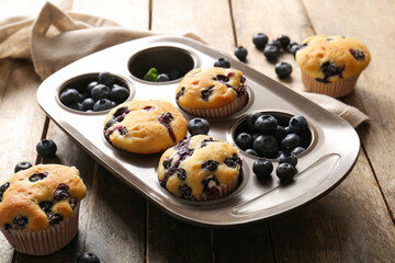 Napkin and baking tray with tasty blueberry muffins on wooden background, closeup