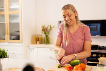 Woman slicing green bell pepper on cutting board at kitchen island, with knife, copy space