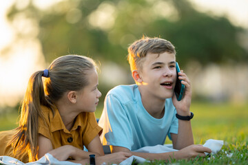 Sad teen friend being ignored by another outdoors while he is talking happily on mobile phone and...