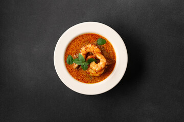 Fresh aromatic hot Thai soup Tom Yum with mushrooms, shrimps and different spices on black stone background top view. Tasty food concept.