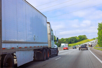 Large truck navigates multi lane American highway with other vehicles under blue sky.