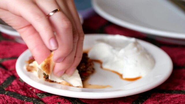 A woman's hand dips a traditional flatbread into a spicy adjika and a fragrant sauce. The perfect photo for culinary projects, travel blogs, and Turkish cuisine ads