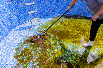 Clean worker removes debris from neglected swimming pool in early spring, preparing it for summer use.