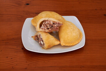 Three fried pastries on a white plate. One of them is cut in half. The plate is on a wooden table