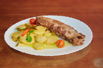 A white plate with a piece of meat and potatoes. The meat is cut into small pieces and is served with a side of potatoes