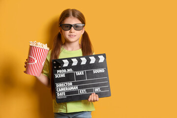Little girl in 3D glasses with popcorn and movie clapper on yellow background