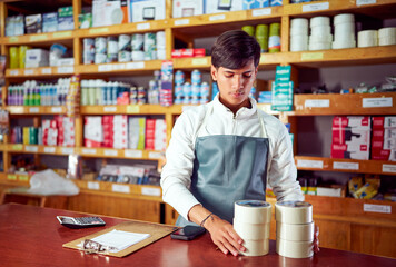 Young hardware store employee organizing adhesive tape stock, ensuring efficient inventory...