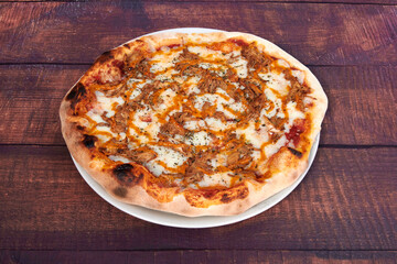 A pizza with meat toppings and cheese on a wooden table. The pizza is on a white plate
