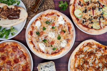 A table with four different pizzas on it. One pizza has a lot of cheese on it