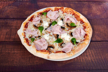 A pizza with ham and mushrooms on a wooden table. The pizza is cut into slices. The table is brown