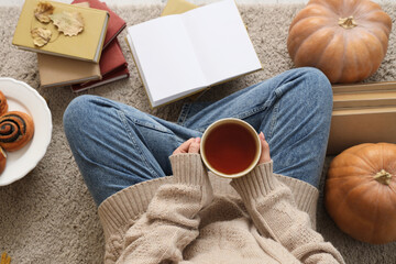 Woman with tea cup, books and buns sitting on carpet at home, top view