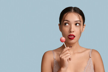 Sexy Asian woman holding sweet lollipop on color background. Erotic concept