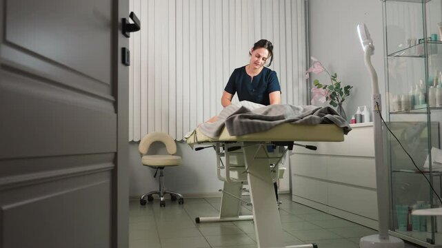 Door view of modern spa room showing aesthetician in uniform with hair tied back massaging back of relaxed client under soft ambient light and neutral d cor for serene wellness experience
