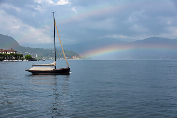 A beautiful view of a yacht on the water with its sails down and a double rainbow behind on Lake Como in Lenno, Lombardy, Italy. Copy space