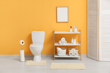 Interior of restroom with toilet bowl, shelving unit and paper holder near yellow wall