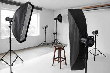 Interior of photo studio with professional equipment, stool and white backdrop