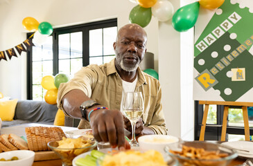 Senior African American man grabbing snack from table at retirement celebration, holding wine glass