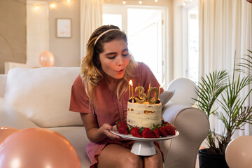 Woman in early thirties sitting in living room blowing out gold 30 candles on birthday cake