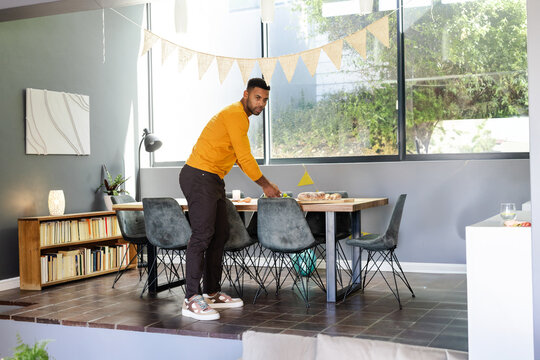 African American man adjusting flag on wooden table in home dining area, with bunting banners