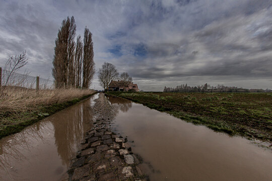 Rural cobblestone road after rainfall. Water surface reflecting cloudy sky.  Increasing humidity due to climate change concept.
