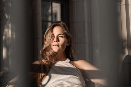 Woman Portrait Sun Light Window - Young woman in a white top posing for a portrait in front of a window with sunlight streaming through.