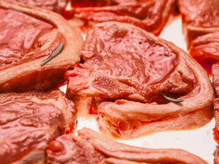 Premium quality marinated lamb loin chops and rosemary herb on white background. Uncooked raw meat on the bone in red color water based marinade to enhance dish taste.