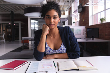 young adult woman organizing red notebook, clipboard and charts on white desk in open-plan office