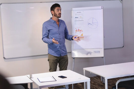 Mid-adult man presenting in meeting room, with flip chart, whiteboard, marker and smartphone