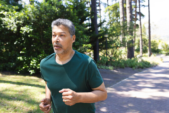 Mature man jogging along paved path in park, wearing dark green shirt and wedding ring