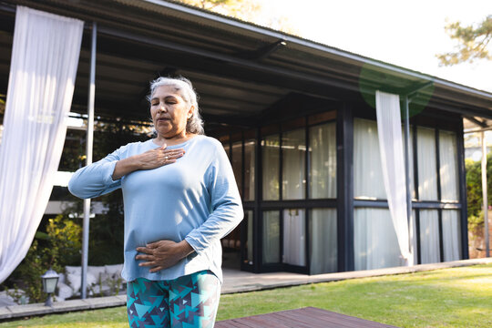 Senior woman practicing mindful breathing on platform on patio, with sheer curtains and lantern