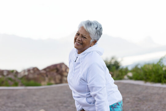 Senior woman leaning forward on gravel path by lake in mountain area, enjoying peaceful scenery