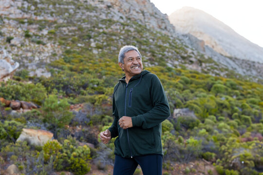 Senior man hiking on rugged mountain trail with low green shrubs, enjoying sunny backcountry
