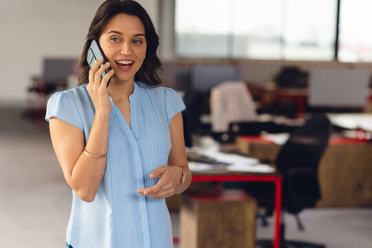 Woman talking on smartphone in office, with gold bangle and wristwatch plus red desks, copy space