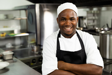 African American chef smiling in professional kitchen, wearing chef's hat and black apron