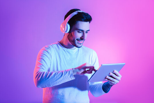 Modern gadgets for joy concept. Happy man in wireless headphones uses tablet