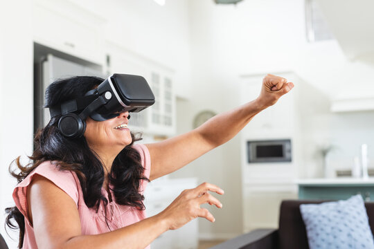 Woman reaching out and engaging with VR headset and headphones in kitchen living area, copy space