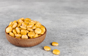 Pickled yellow lupine beans in a wooden bowl on a grey background. Copy space. High protein plant food.