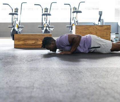 African American man lying on gray exercise mat at gym, with stationary bikes and wooden boxes