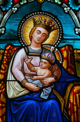 Fototapeta premium Stained glass (1913) of Blessed Virgin Mary holding baby Jesus Christ in her arms.